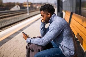 enojado hombre con un maleta y móvil teléfono sentado en un banco a el ferrocarril estación. foto