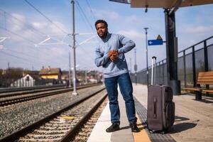preocupado hombre mirando a su reloj mientras en pie con maleta en un ferrocarril estación. foto