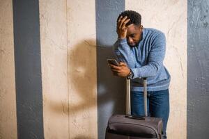 Worried man with suitcase and mobile phone leaning against a wall in passage of the railway station. Copy space on image for your advert or text. photo