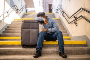 Worried man with a phone and suitcase sitting on a stairs at the railway station. photo