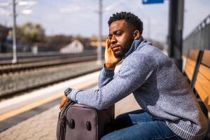 preocupado hombre con un maleta sentado en un banco a el ferrocarril estación. foto