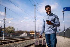 Happy man with a suitcase using phone while standing on the railway station photo