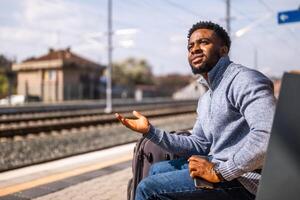 enojado hombre con un maleta y móvil teléfono sentado en un banco a el ferrocarril estación. foto