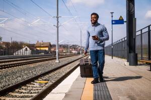 contento hombre con un maleta utilizando teléfono mientras caminando en el ferrocarril estación. foto