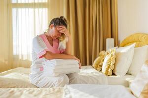 Image of sad overworked hotel maid sitting on the bed in a room. photo