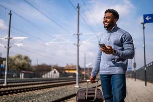 Happy man with a suitcase using phone while standing on the railway station photo