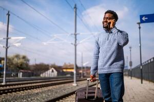 contento hombre con un maleta es hablando en el teléfono mientras en pie en el ferrocarril estación. foto