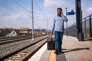 contento hombre con un maleta es hablando en el teléfono mientras caminando en el ferrocarril estación. foto