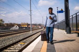 contento hombre con un maleta utilizando teléfono mientras caminando en el ferrocarril estación. foto