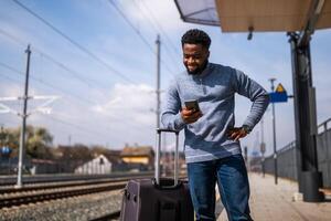 enojado hombre con un maleta y móvil teléfono en pie en un ferrocarril estación. foto