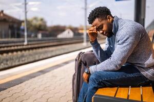 Worried man with a suitcase sitting on a bench at the railway station. photo