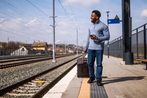 contento hombre con un maleta utilizando teléfono mientras caminando en el ferrocarril estación. foto