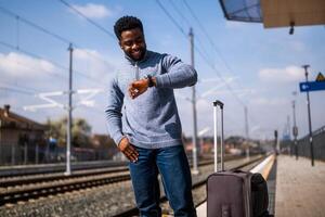 contento hombre mirando a su reloj mientras en pie con maleta en un ferrocarril estación. foto