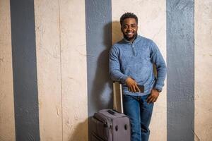 Happy man with suitcase using phone while leaning against a wall in passage of the railway station. Copy space on image for your advert or text. photo