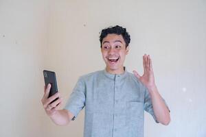 musulmán asiático hombre contento durante llamada con teléfono inteligente cuando Ramadán celebracion. foto