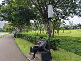 hombre sentar en el verde parque abajo ciudad. el foto es adecuado a utilizar para calma disfruté actividad, ocio actividad y parque antecedentes.