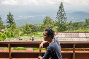 Man sitting near fence and looking the landscape mountain. The photo is suitable to use for calm enjoyed activity, leisure activity and park background.