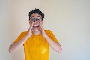 Young man wear glasses and yellow t-shirt shouting. The photo is suitable to use for man expression advertising and fashion life style.