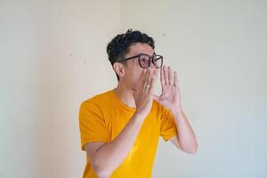 Young man wear glasses and yellow t-shirt shouting. The photo is suitable to use for man expression advertising and fashion life style.