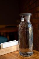 botella de agua en un de madera mesa en contra el antecedentes de un ladrillo pared en un cafetería, de cerca foto