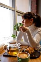 un joven mujer sentado en un café y Bebiendo té, mirando fuera el ventana y esperando para su compañero foto