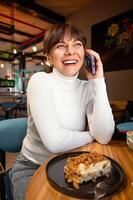 Portrait of a broadly laughing woman talking on the phone while sitting in a cafe, lunch break photo