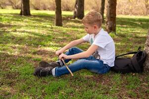 un chico con un palo se sienta en el césped en un primavera parque foto