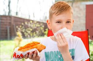 A boy eats a hotdog at a table in a cafe in a spring park photo