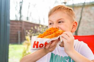 A boy eats a hotdog at a table in a cafe in a spring park photo