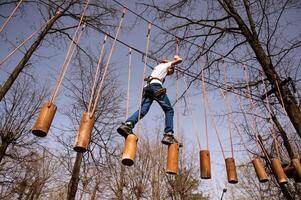 A boy in a helmet climbs a rope park in the spring photo