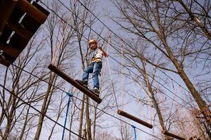 A boy in a helmet climbs a rope park in the spring photo