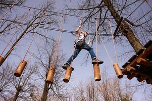 A boy in a helmet climbs a rope park in the spring photo