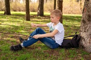 un chico con un palo se sienta en el césped en un primavera parque foto