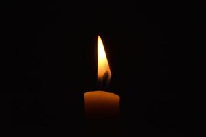 Single Candle with flame in the dark place, isolated black background photo