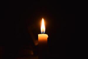 Single Candle with flame in the dark place, isolated black background photo