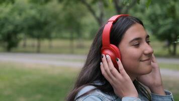 Lycklig Lycklig flicka i denim kläder dans i de parkera nära de träd under de dag lyssnande till glad musik i hörlurar. roligt humör. närbild video