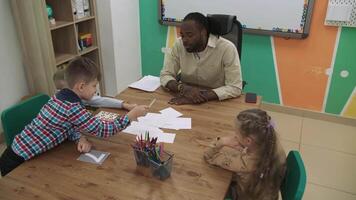 afrikansk amerikan lärare och en grupp av barn är inlärning tal medan Sammanträde på de tabell i de klassrum.skola för barn, undervisning tonåringar, få kunskap, lära sig de språk. video