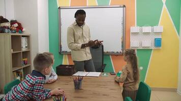 een Afrikaanse Amerikaans leraar geeft les een groep van kinderen in de klas in een speels manier.school voor kinderen, onderwijs adolescenten, krijgen kennis, leren de taal. video