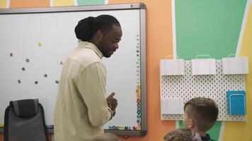 un africano americano profesor y un grupo de niños son estudiando frutas y animales en el aula.escuela para niños, enseñando adolescentes, ganancia conocimiento, aprender el idioma. video