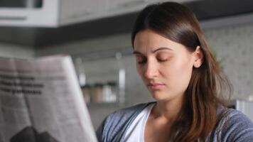 giornale notizia. mondo pandemia. fonte di notizia. leggere giornale. bellissimo donna legge un' fresco notizia giornale mentre seduta a casa nel il cucina. avvicinamento video