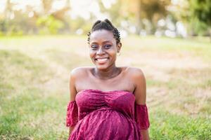 Happy African pregnant woman smiling on camera in a public park - Maternity lifestyle concept photo