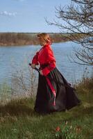 A woman with short red hair in black and red hanfu and a katana on the background of a river in spring photo