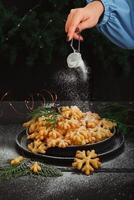 A woman's hand sprinkles powdered sugar on a sweet treat brushwood in the form of snowflakes photo