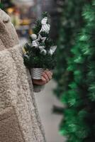 un mujer en un piel Saco con un pequeño artificial Navidad árbol en su manos en un Tienda foto