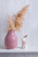 The decor elements of a bright room in an eco-style are a shelf with a pink vase, a reed and a porcelain rabbit photo