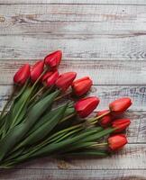 Red tulips with leaves lie on a wooden background photo