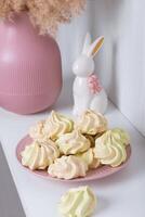 Sweet treat for the holiday - meringue on a plate on the background of a vase and a porcelain rabbit photo