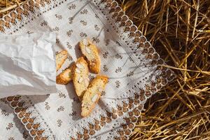 Almond cookies crackers with pieces of nuts fell out of a paper bag on a napkin lying on the straw, top view photo