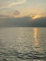 hermosa puesta de sol en el mar, el Dom conjuntos detrás un grande nube acostado en el agua foto