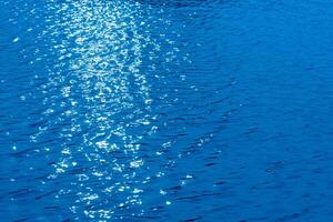 Bluewater waves on the surface ripples blurred. Defocus blurred transparent blue colored clear calm water surface texture with splash and bubbles. Water waves with shining pattern texture background. photo